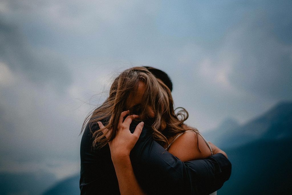 Person with flowing hair photographed against mountainous backdrop and moody sky.