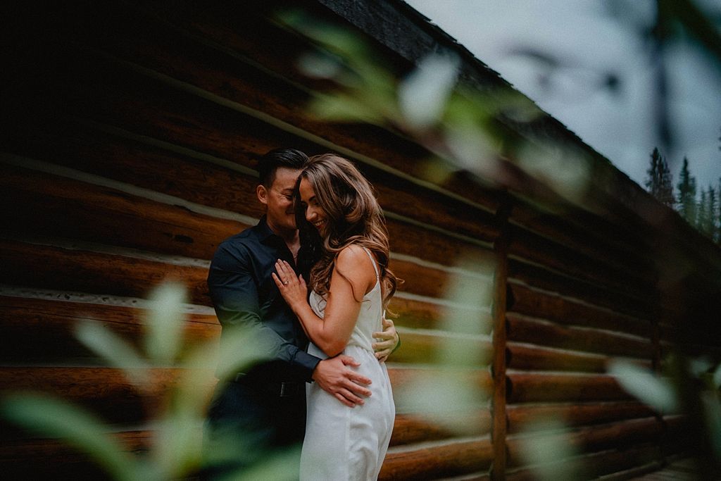 Couple embraces on a wooden deck surrounded by forest greenery.