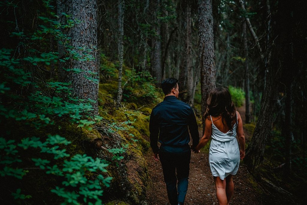Couple walking hand in hand down a winding forest trail.
