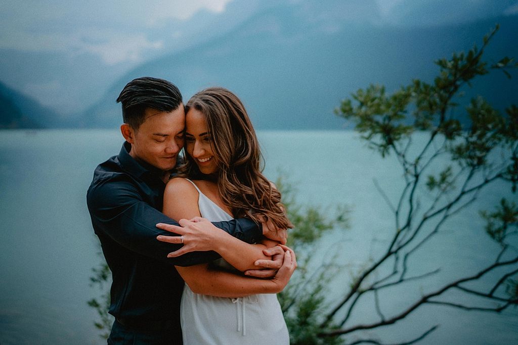 Couple embraces by a misty mountain lake during an intimate photoshoot.