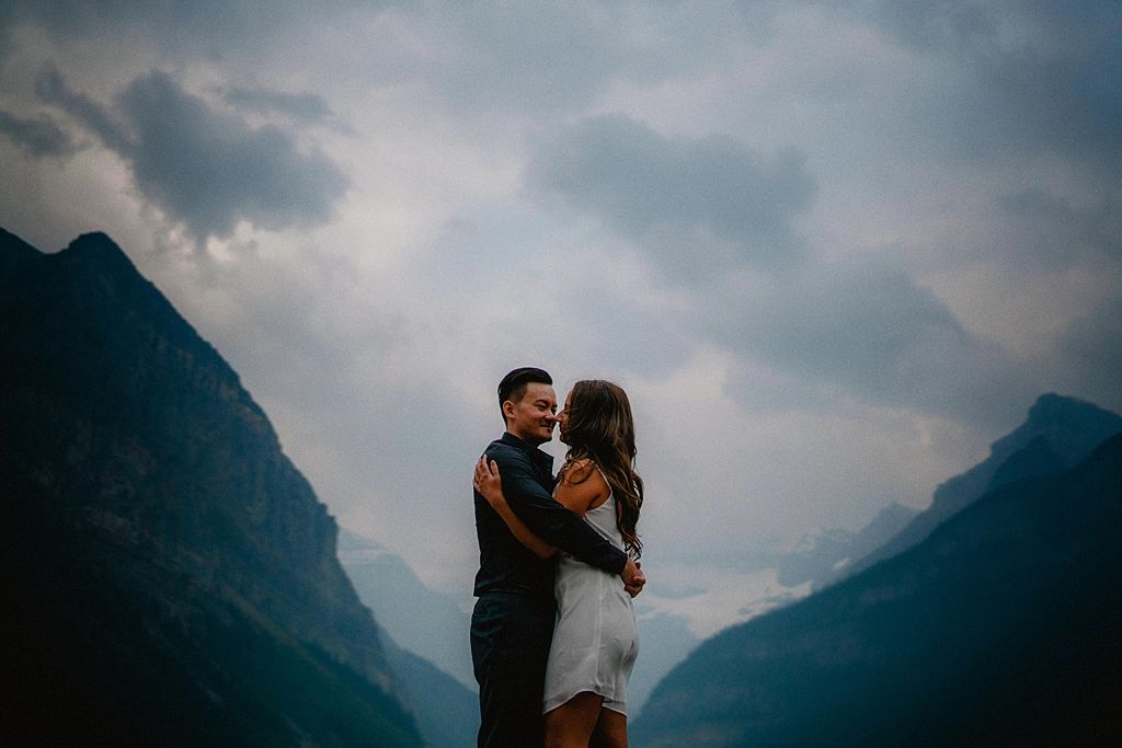 Couple in dramatic mountain valley with cloudy skies during engagement shoot.