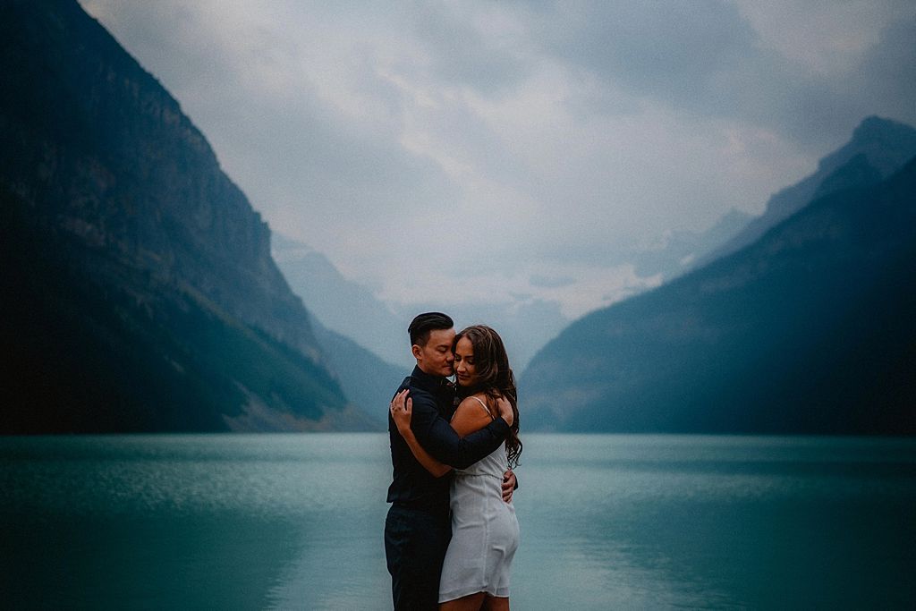 A couple shares an intimate moment by a turquoise alpine lake surrounded by majestic mountains.