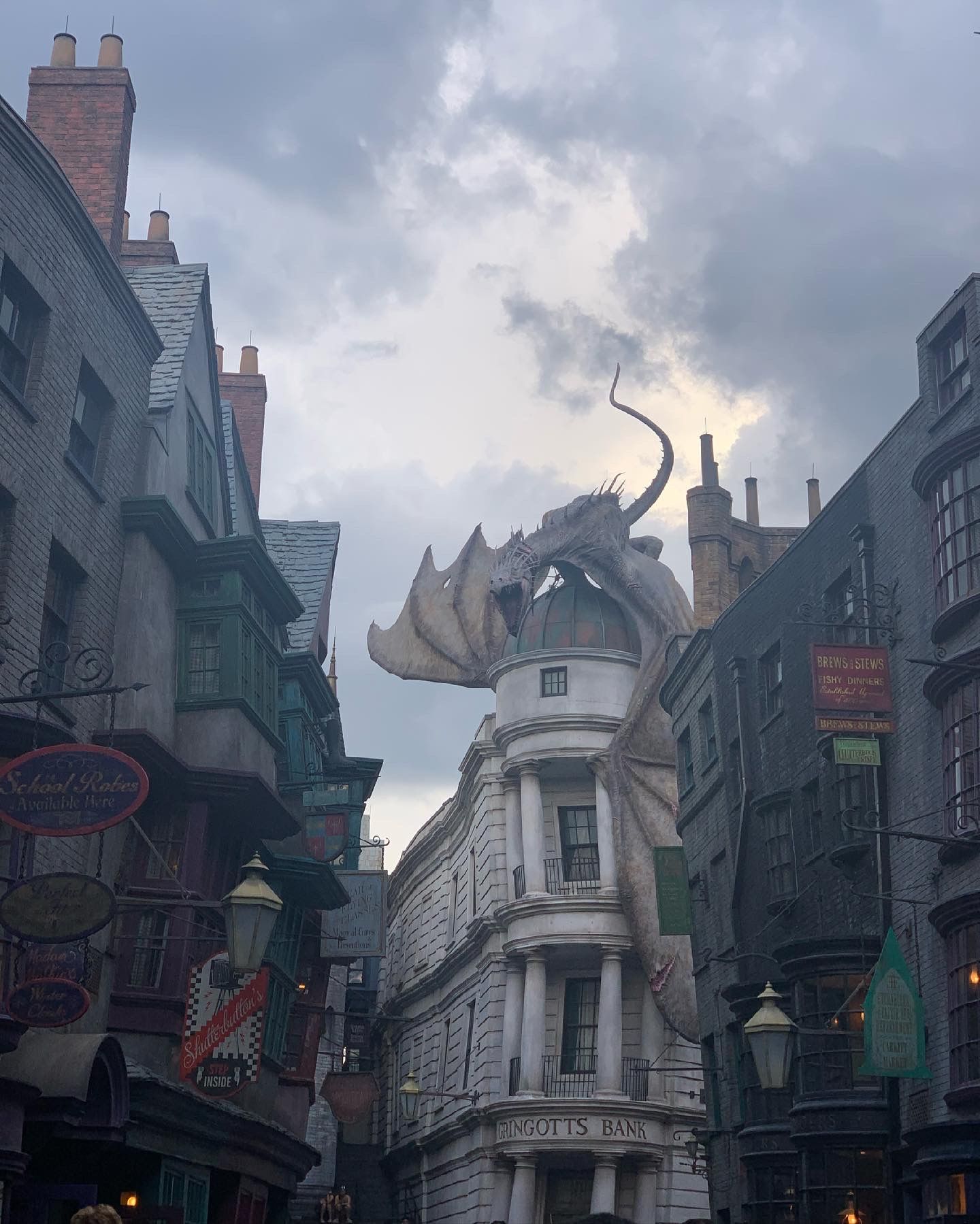 A dragon statue perched atop a building in The Wizarding World theme park against a cloudy sky.
