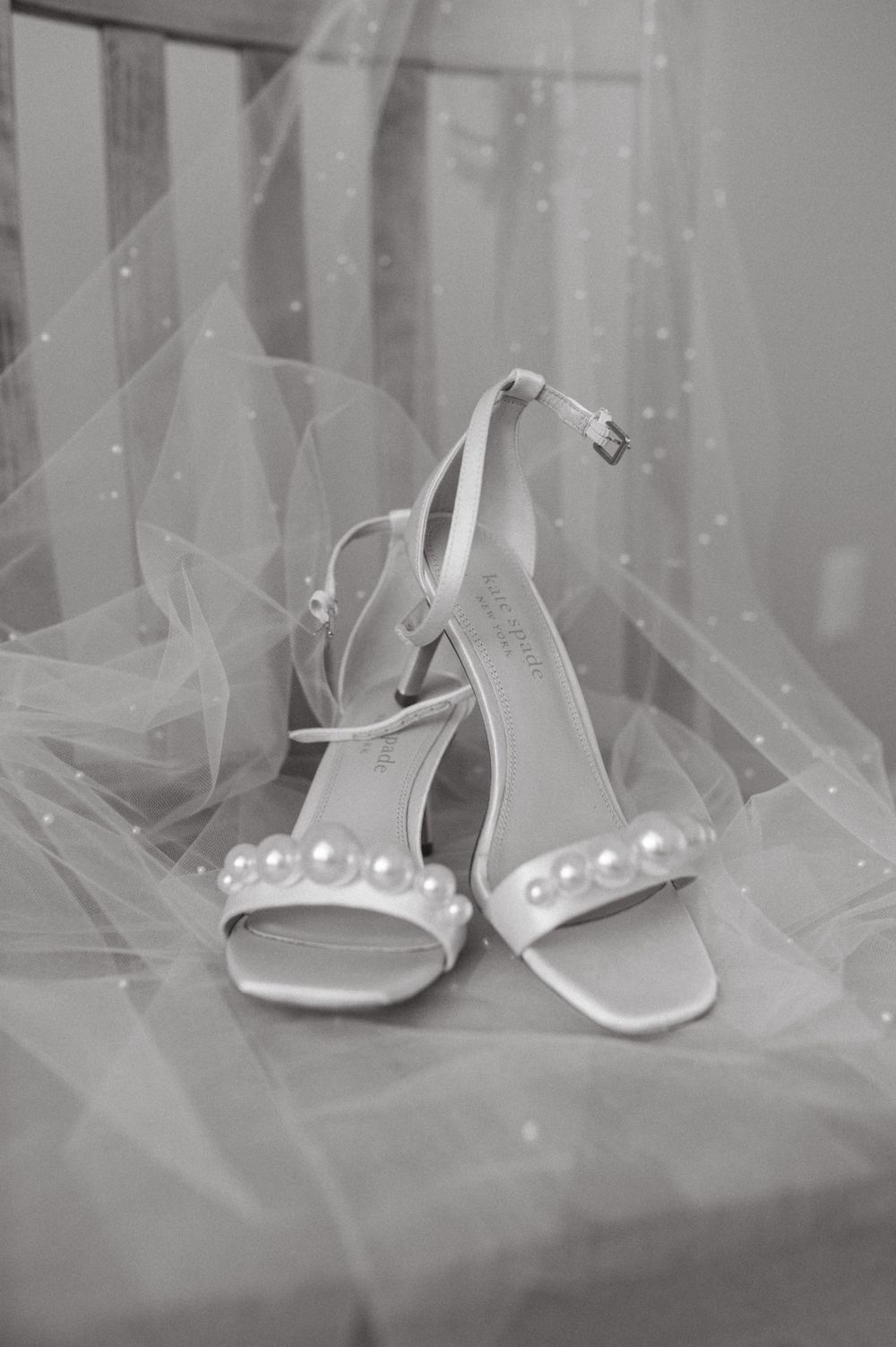Elegant white bridal shoes with pearl details resting on delicate tulle fabric.
