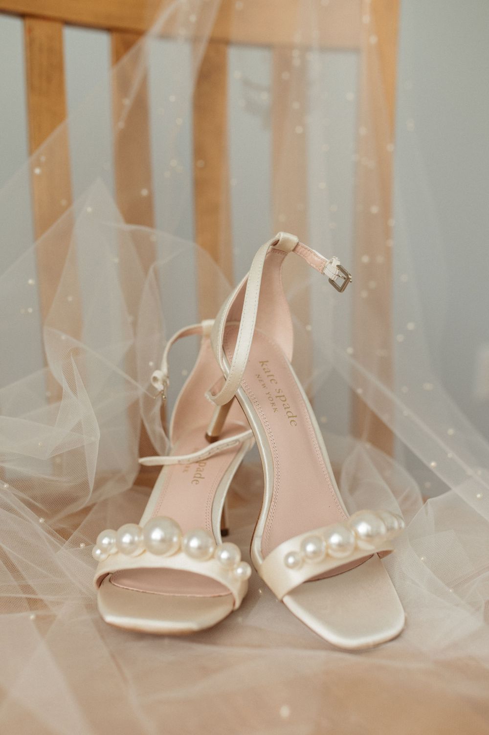 Pearl-adorned white bridal sandals displayed against sheer tulle fabric.