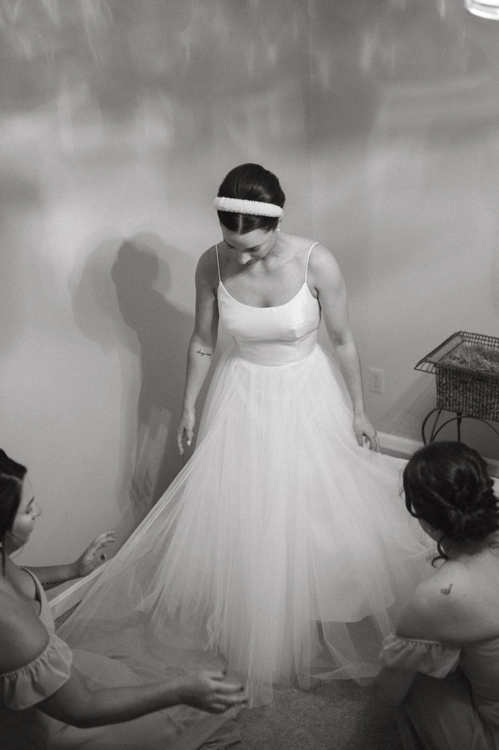 Wedding preparations scene with assistants helping adjust a flowing white gown.