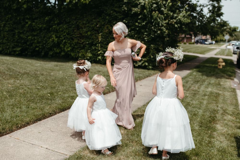 Young flower girls in white tulle dresses walking with an attendant in a blush gown.