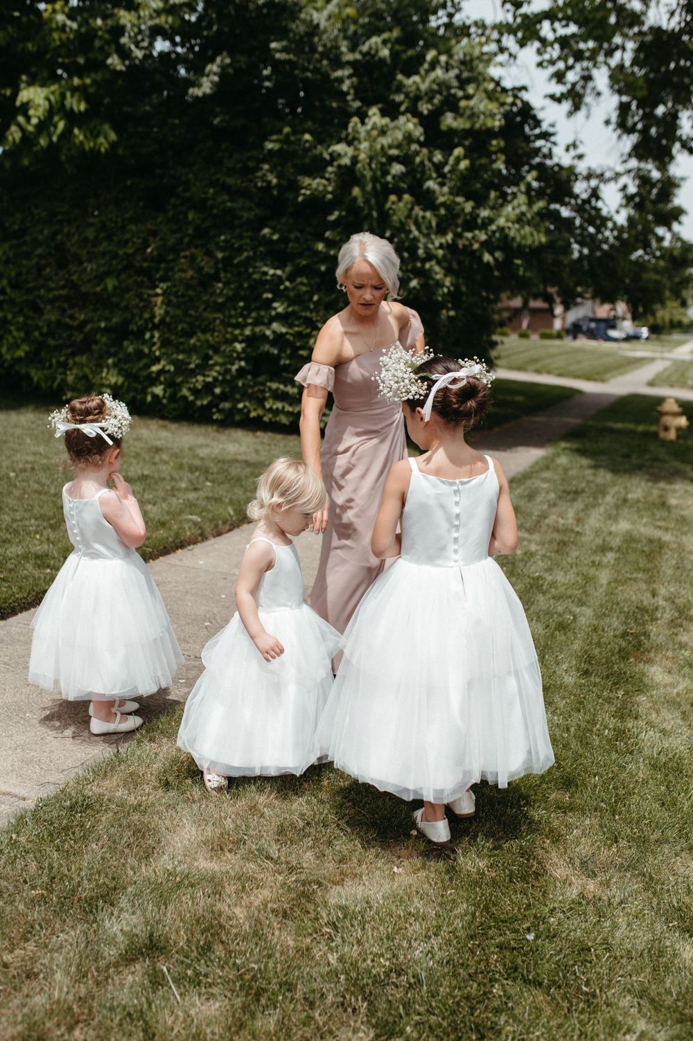 Three attendants in white and blush dresses walking along an outdoor path.