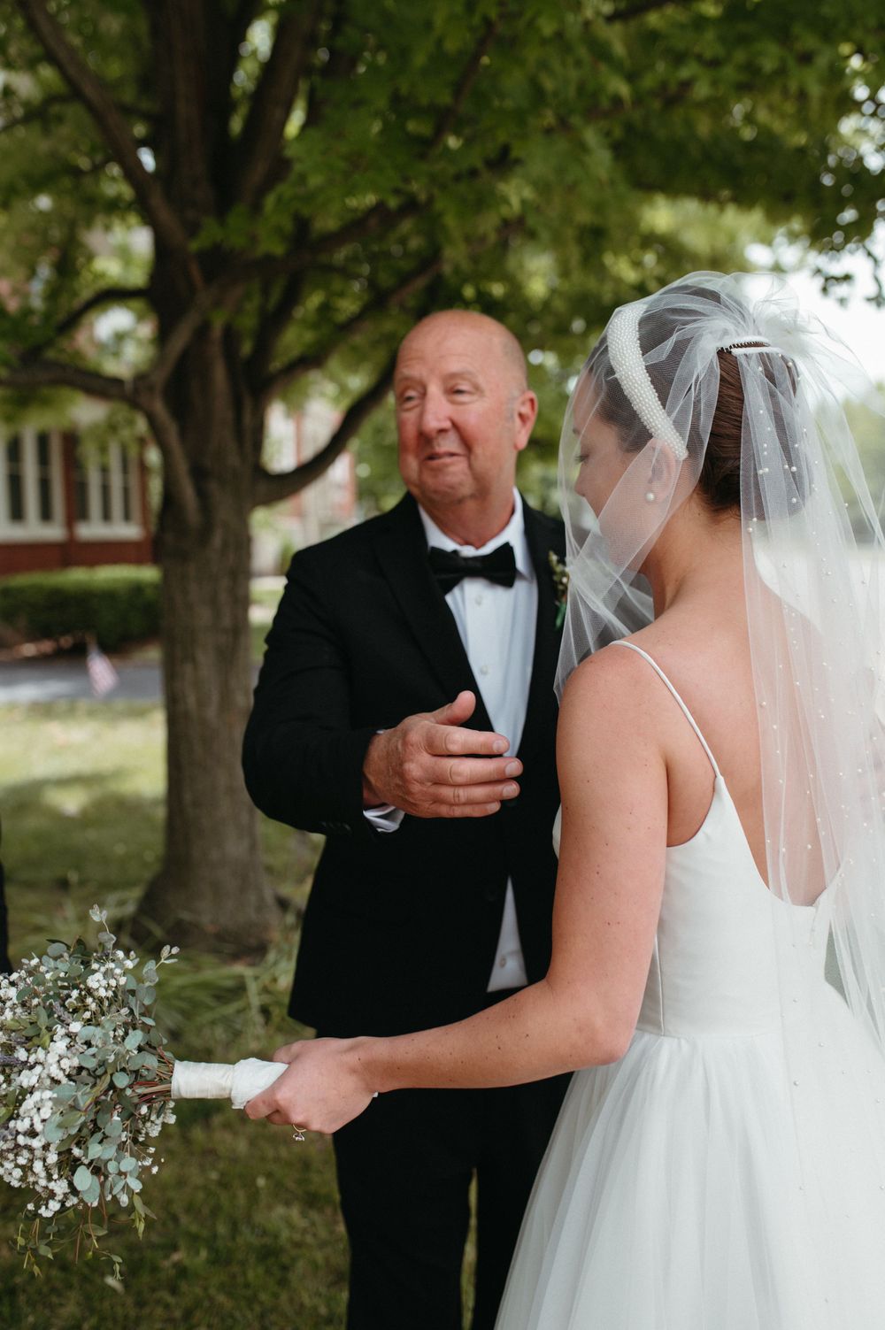 A tender wedding moment shared between a bride and person in formal attire outdoors.