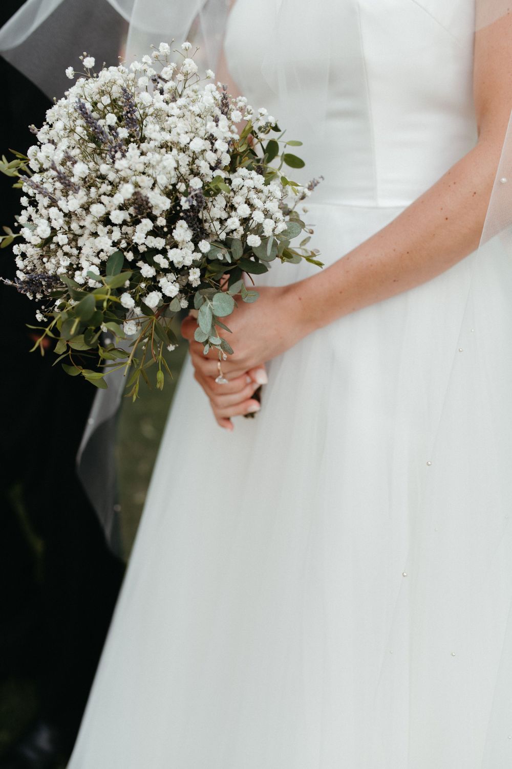 A close-up of a bride holding a delicate white baby's breath and eucalyptus bouquet.