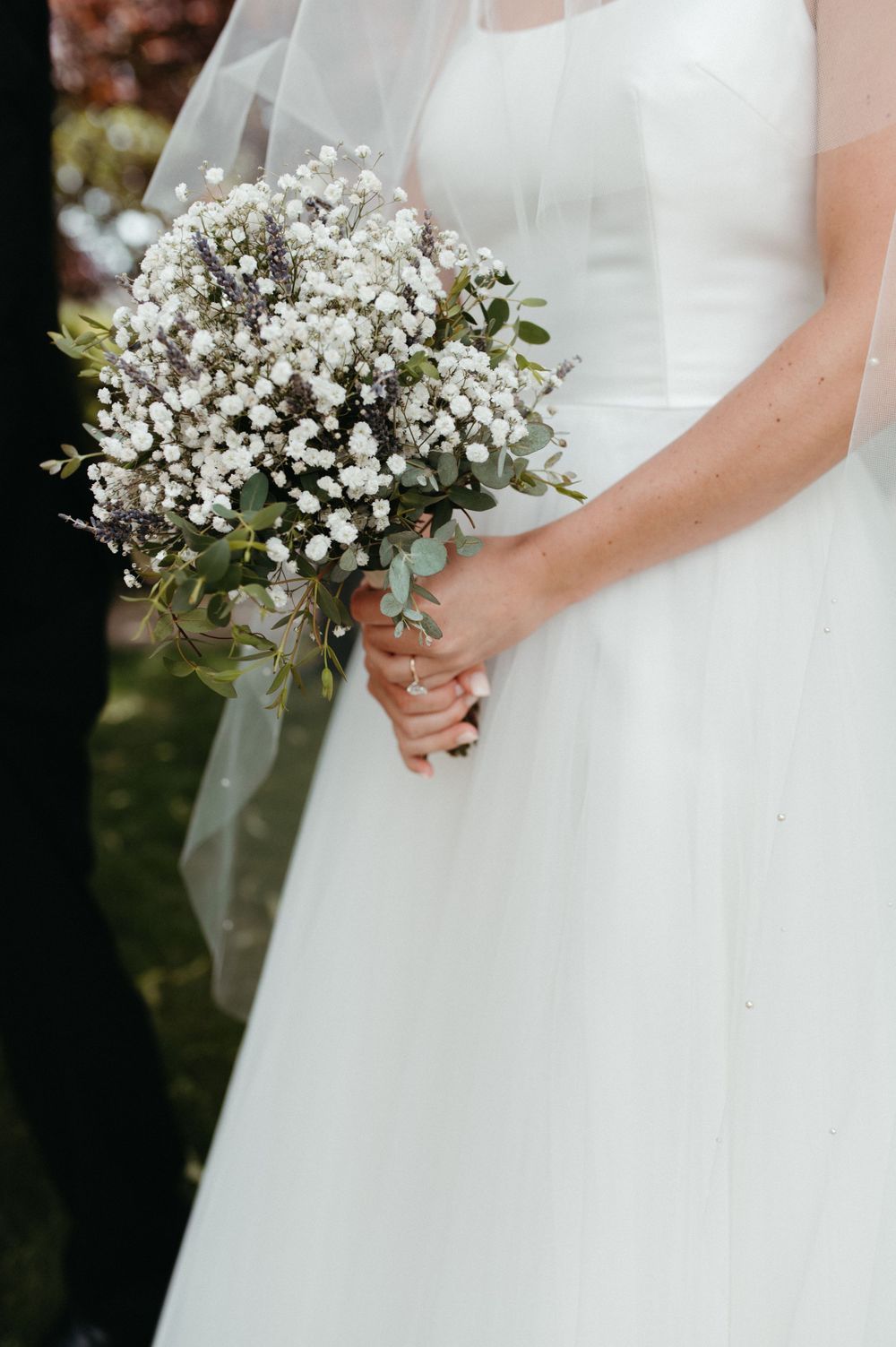 Detail shot of white wedding bouquet with baby's breath and eucalyptus against a bridal gown.