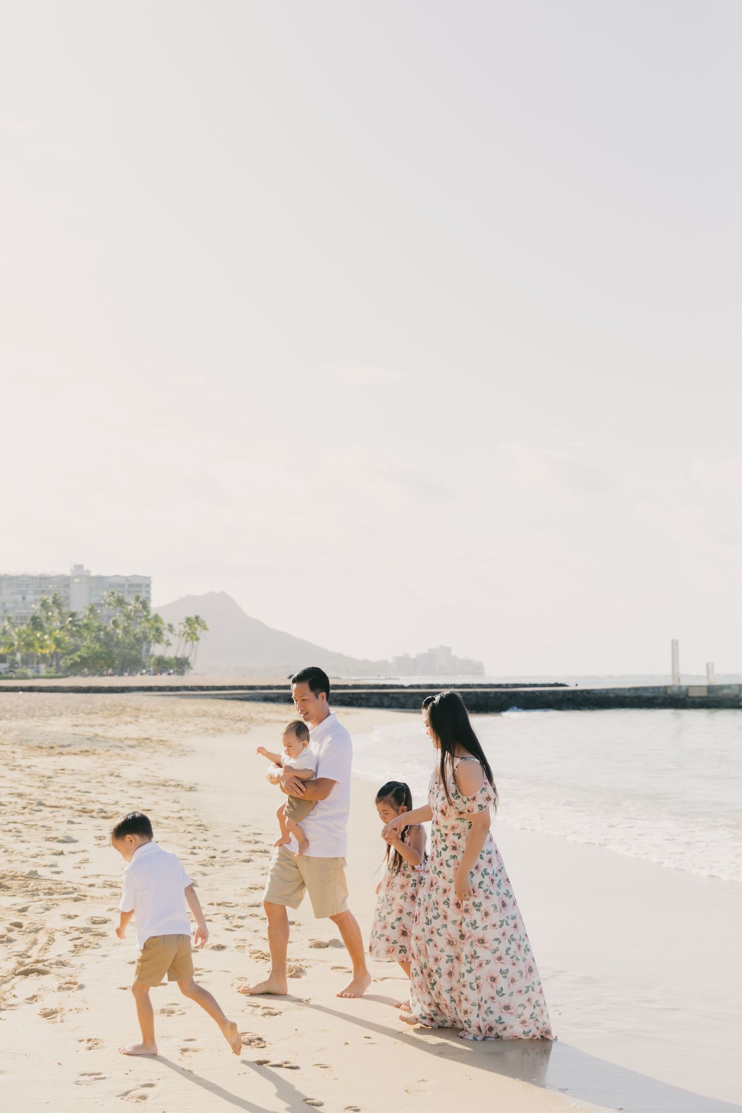 Family walking together on a sunny beach with mountains in the background.