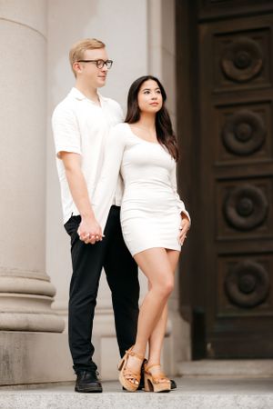 Stylish couple poses by ornate doorway in coordinated black and white outfits.