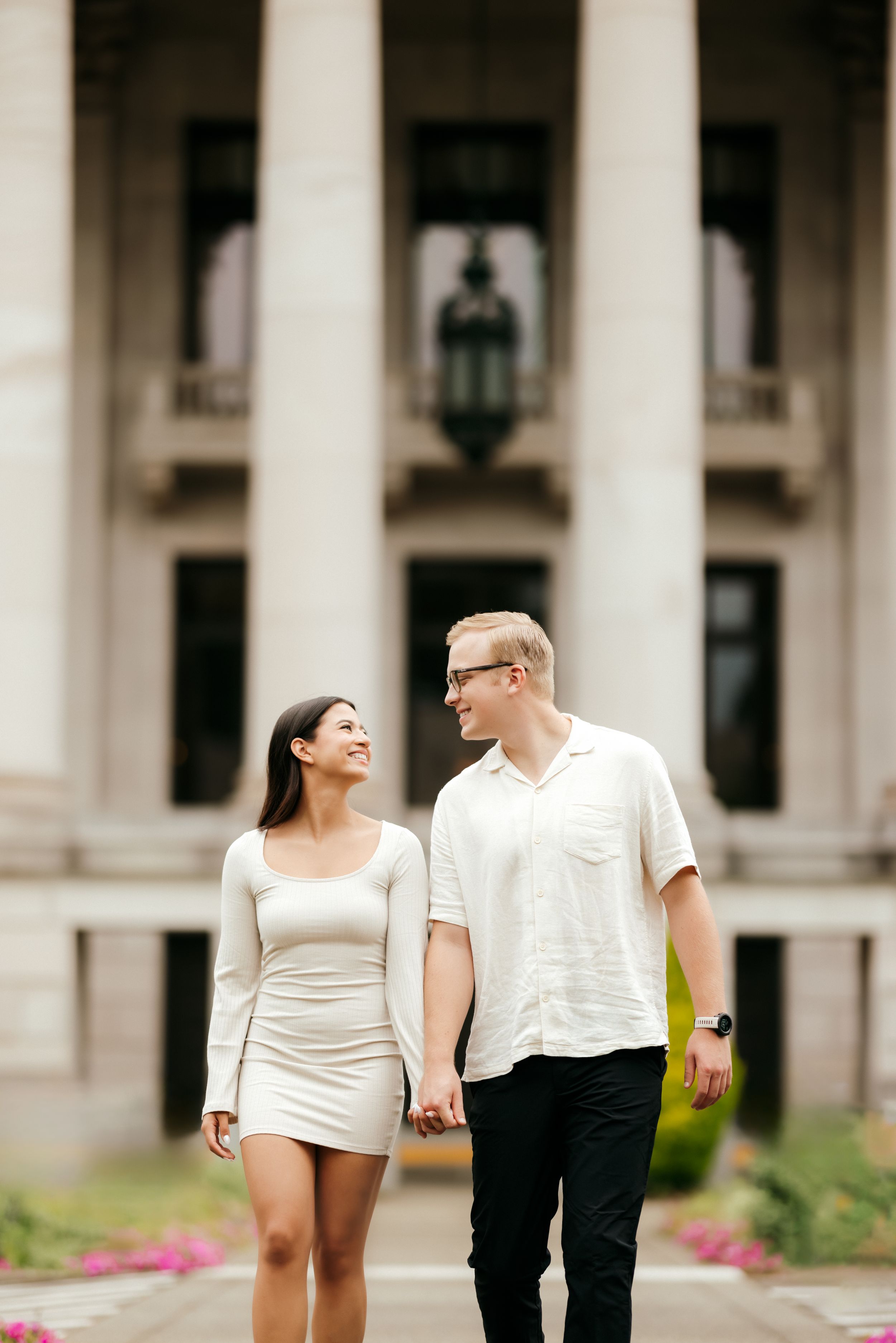 A couple holding hands and smiling while walking in front of a grand columned building.