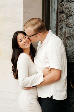 Joyful couple sharing intimate moment against white wall during portrait session.