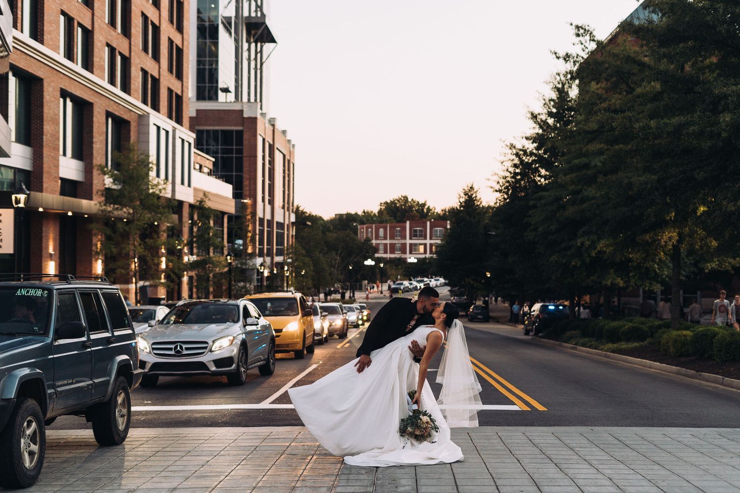 Bride and wedding party walking down a city street with flowing dress trailing behind.