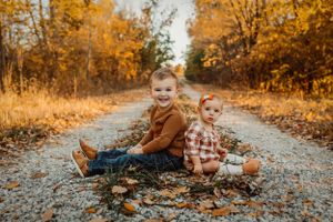 Family lying on a gravel path surrounded by autumn foliage during sunset.