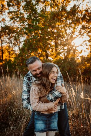 A couple embraces and laughs together in tall grass during golden hour.