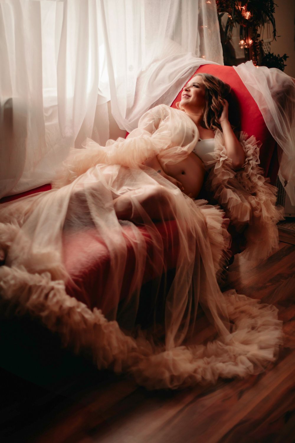 Dreamy maternity portrait with ethereal tulle fabric in a sunlit room.