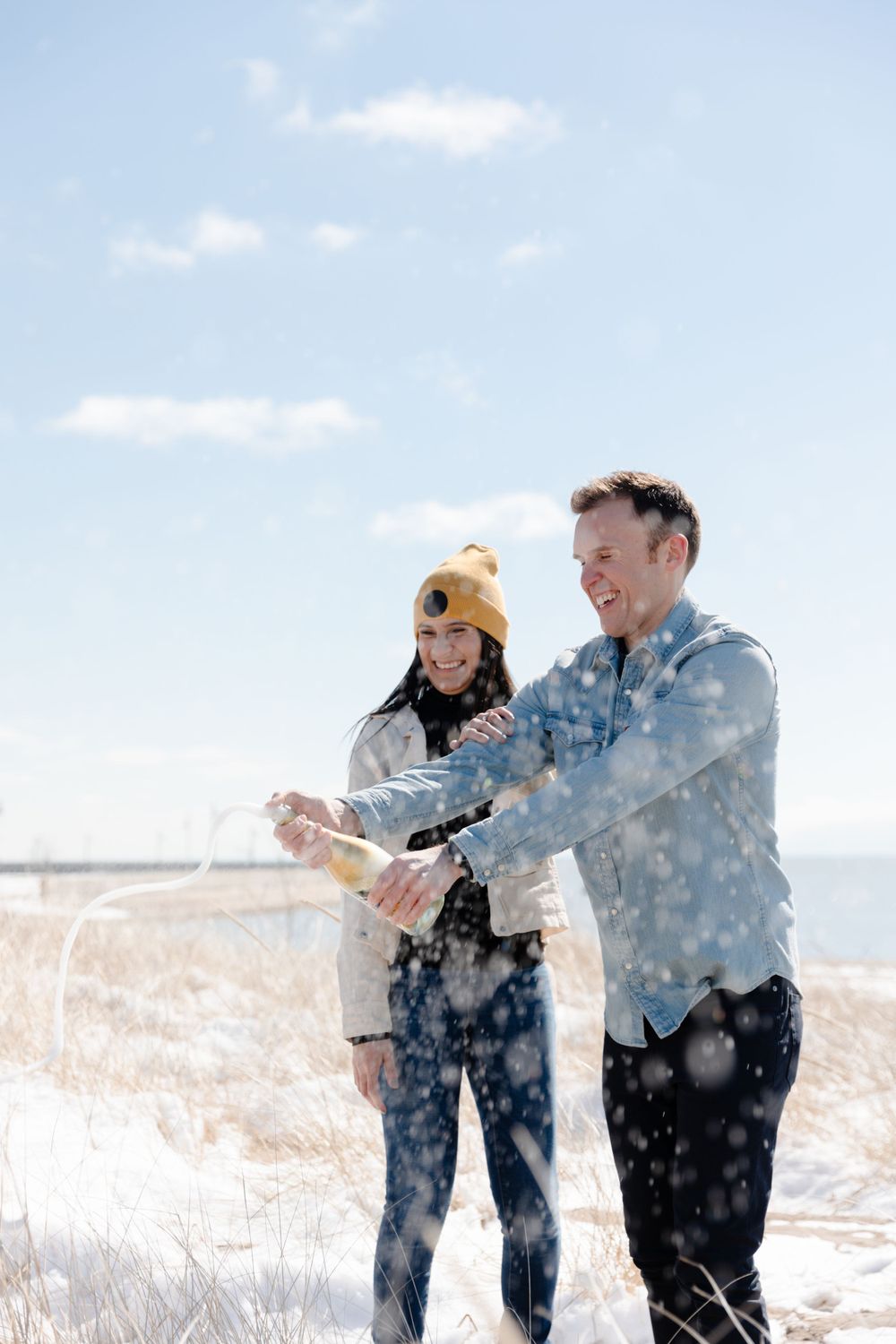 A man and woman are holding a bottle of champagne in the snow.