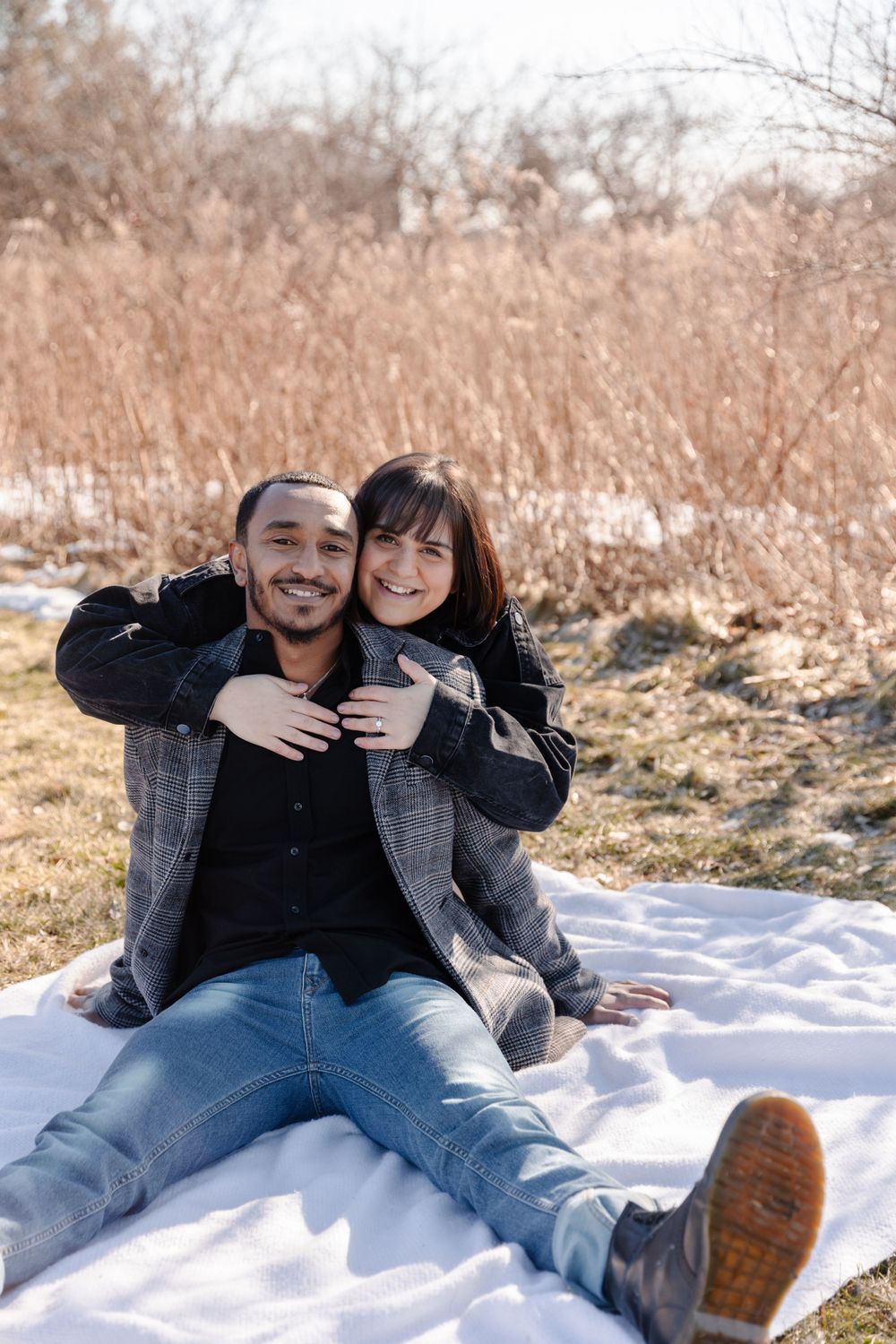 A couple laying on a blanket in a field.