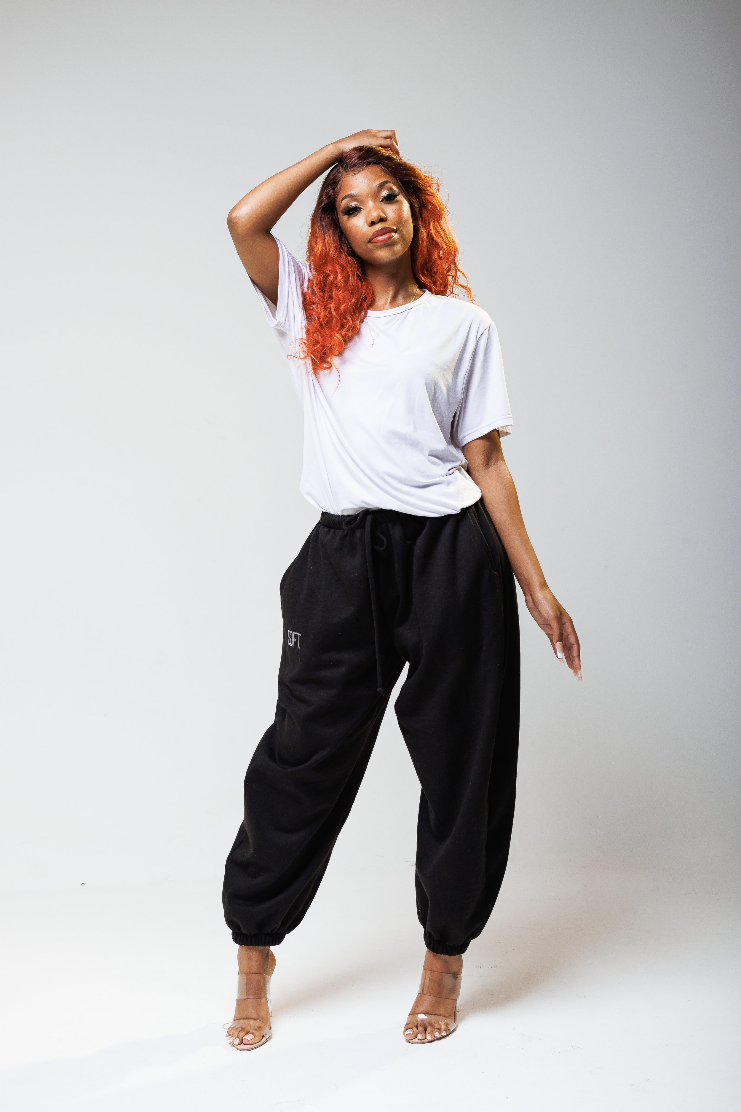 Model in casual white t-shirt and black joggers strikes dynamic pose against white backdrop.