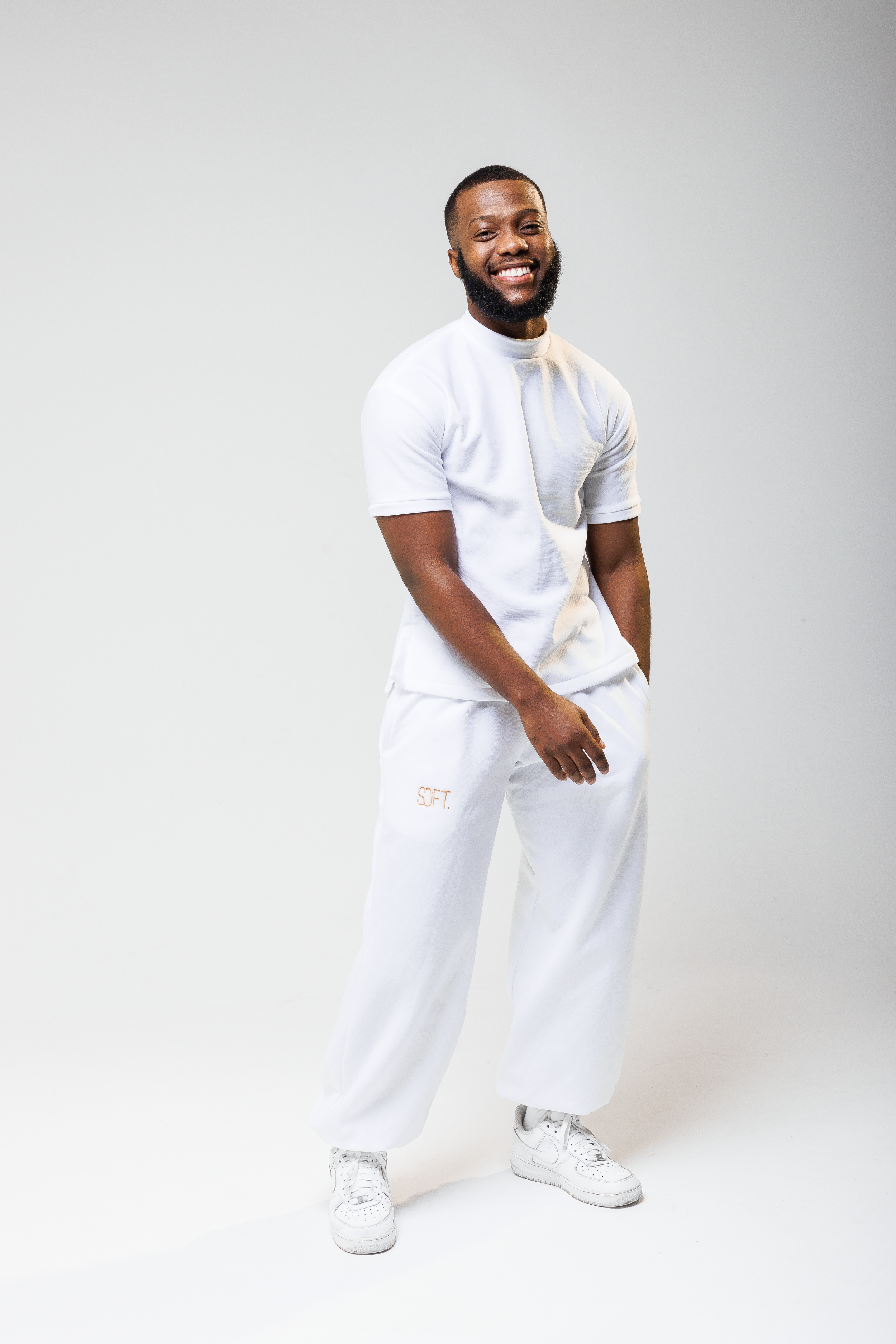 Person wearing all-white athletic outfit strikes confident pose against light gray background.