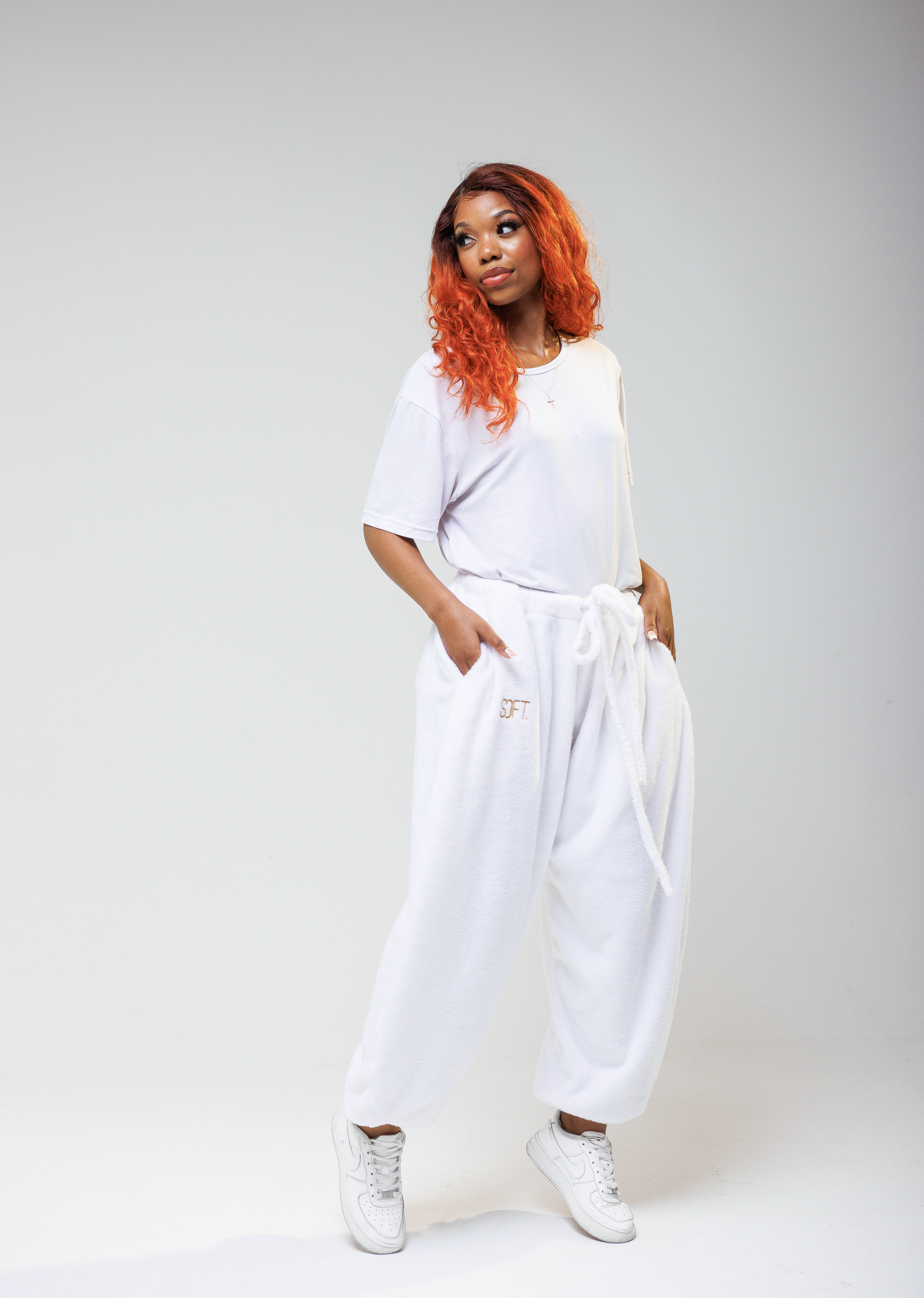 Model in white activewear outfit poses casually with hands in pockets.