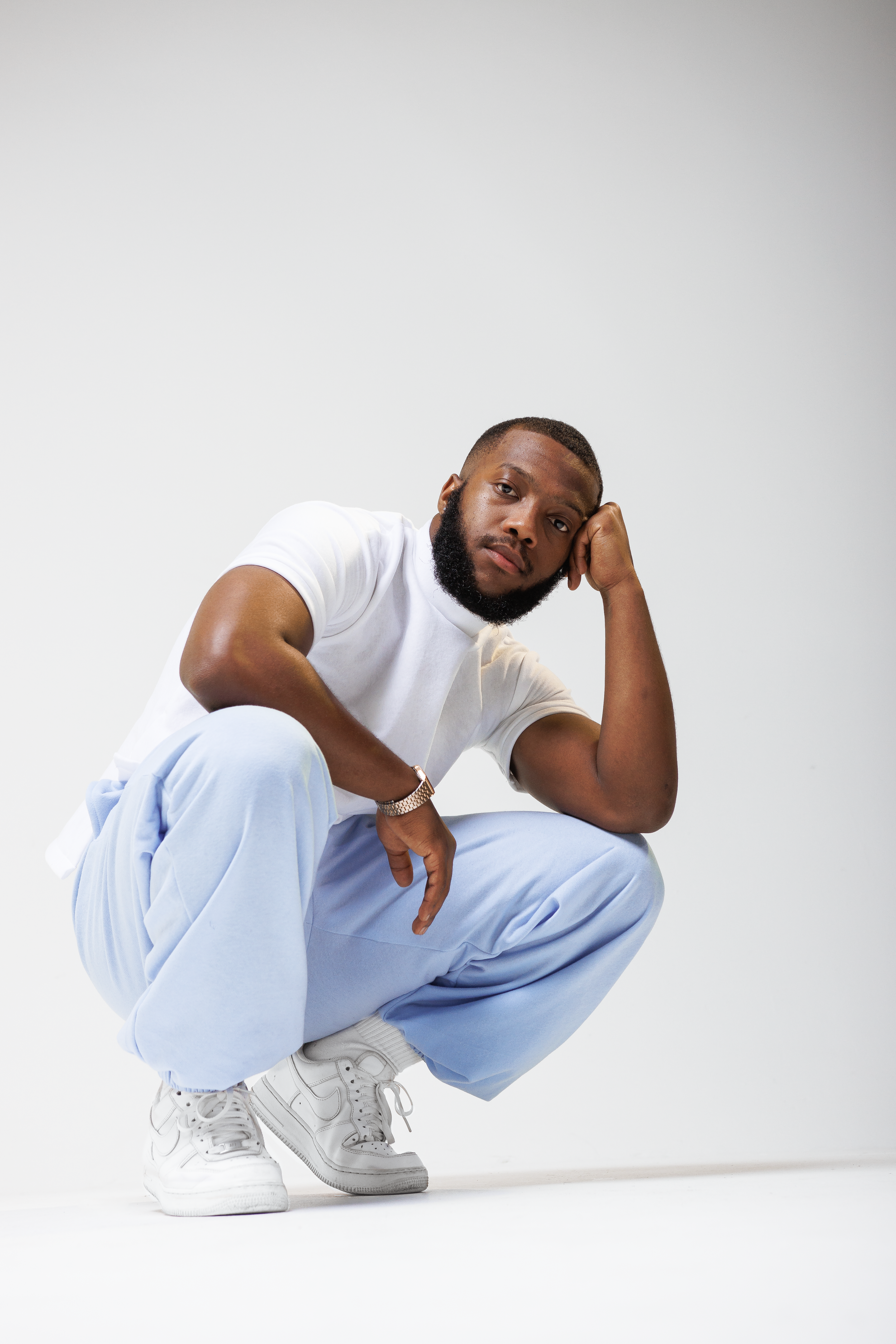 Model in white t-shirt and light blue pants crouches in thoughtful pose.