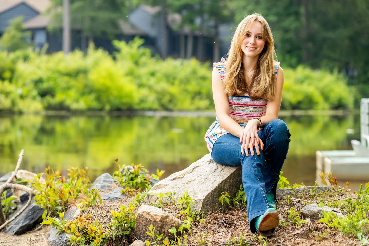 Person relaxing on a log by a serene pond surrounded by lush greenery.