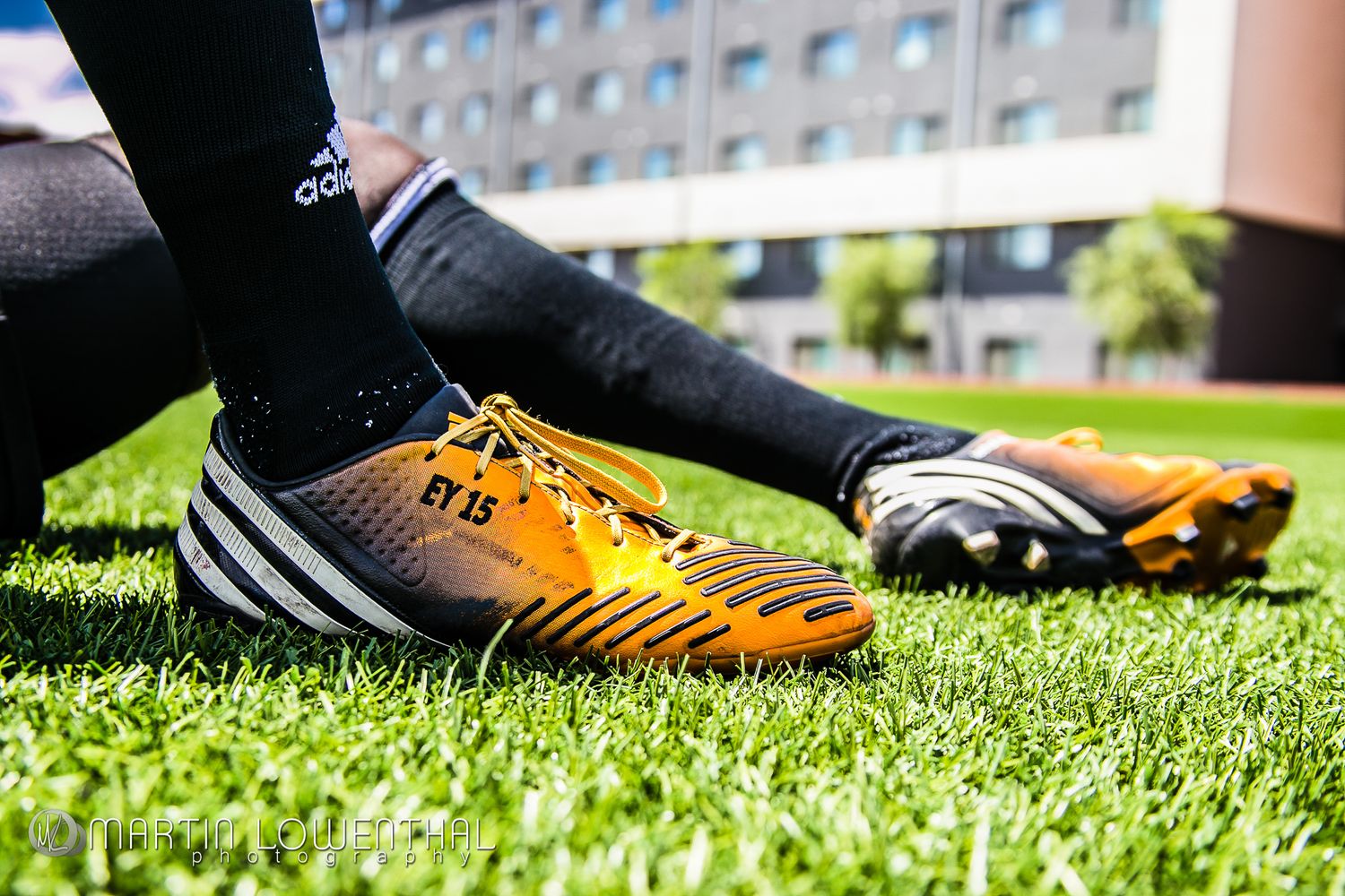 Close-up of orange and black Adidas soccer cleats on grass field.