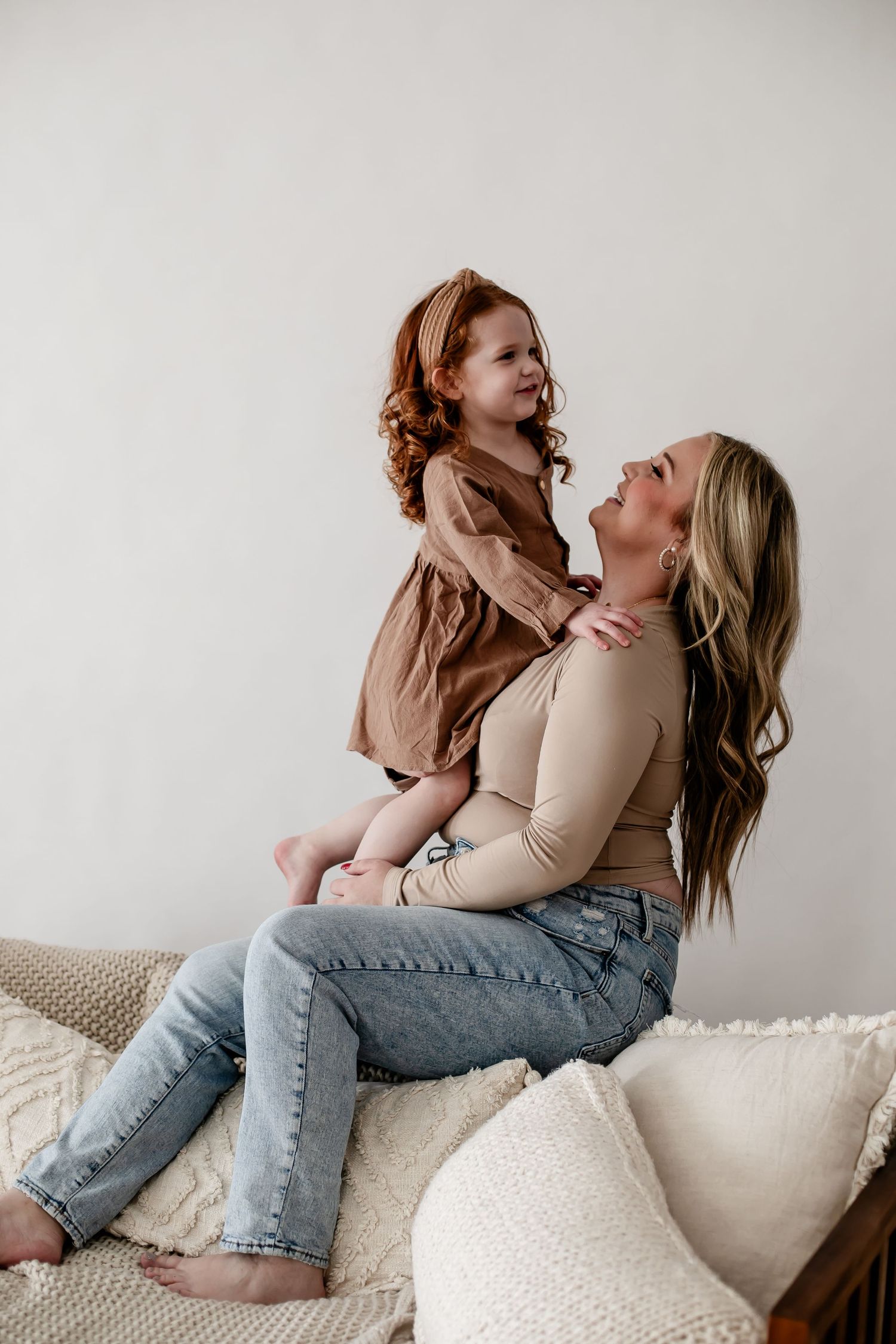Playful lifestyle portrait of parent lifting child on white couch.