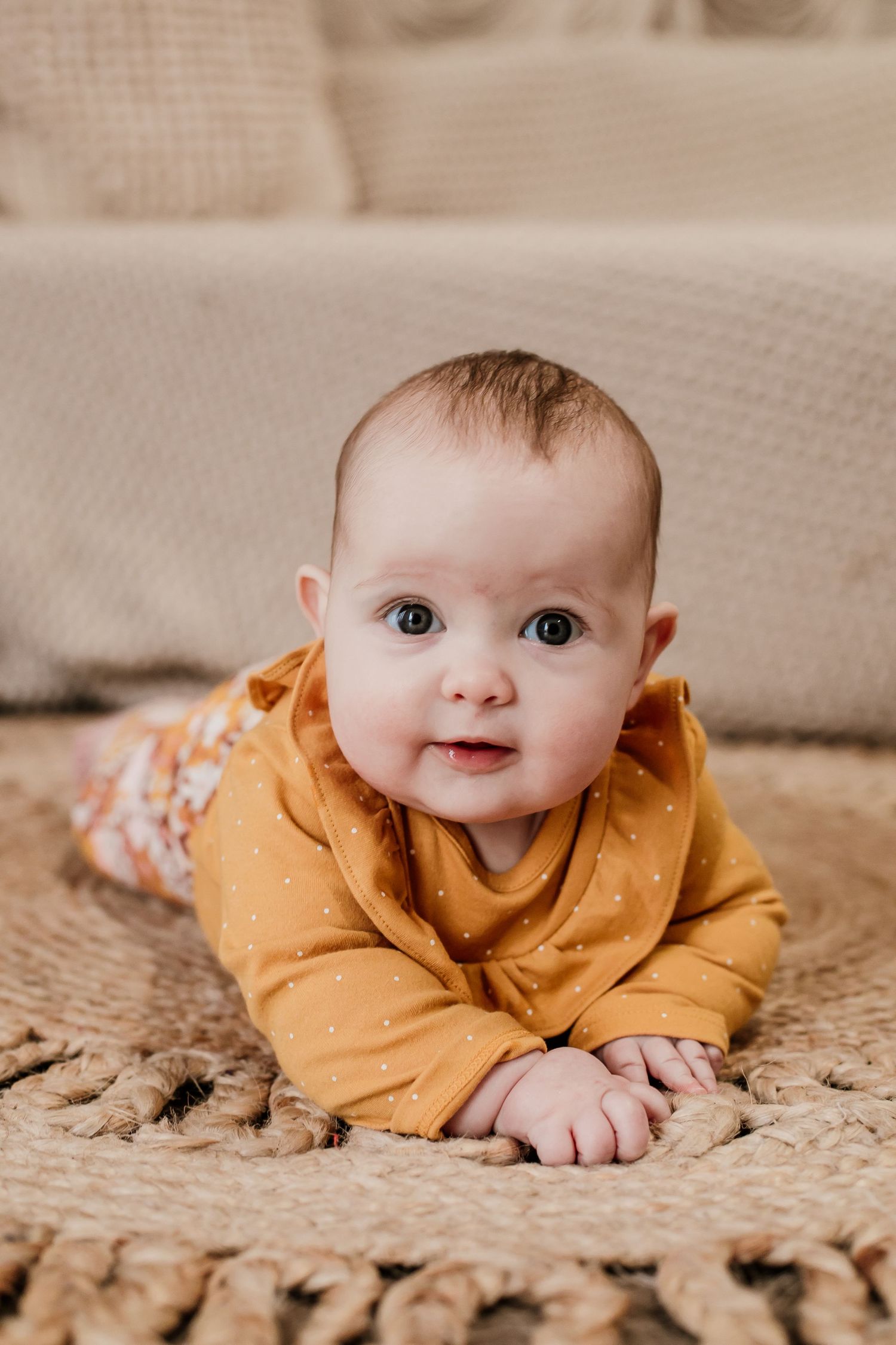 Baby in mustard yellow outfit crawling on textured carpet with bright expression.