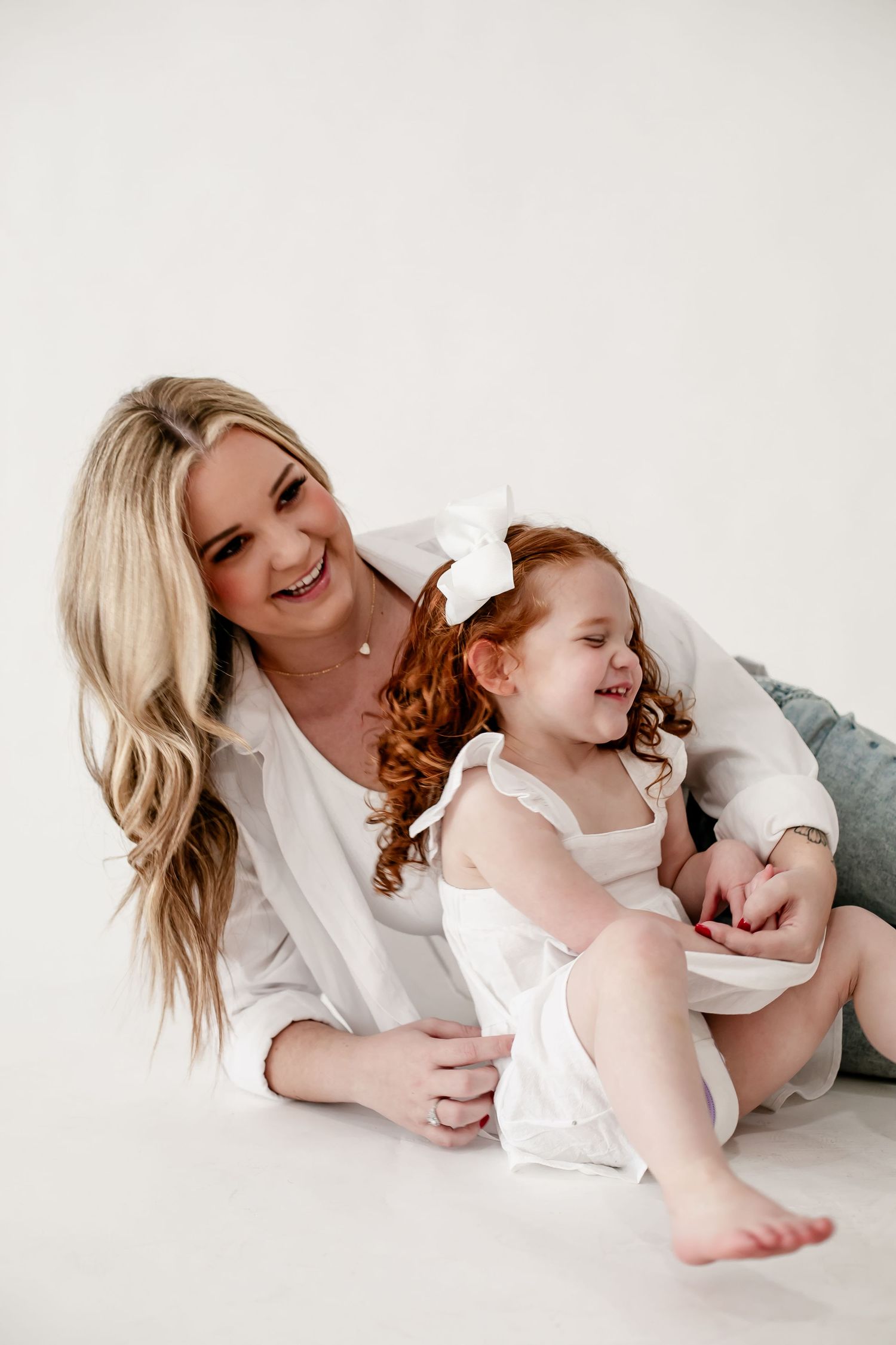 Parent and child sharing playful moment on white floor.