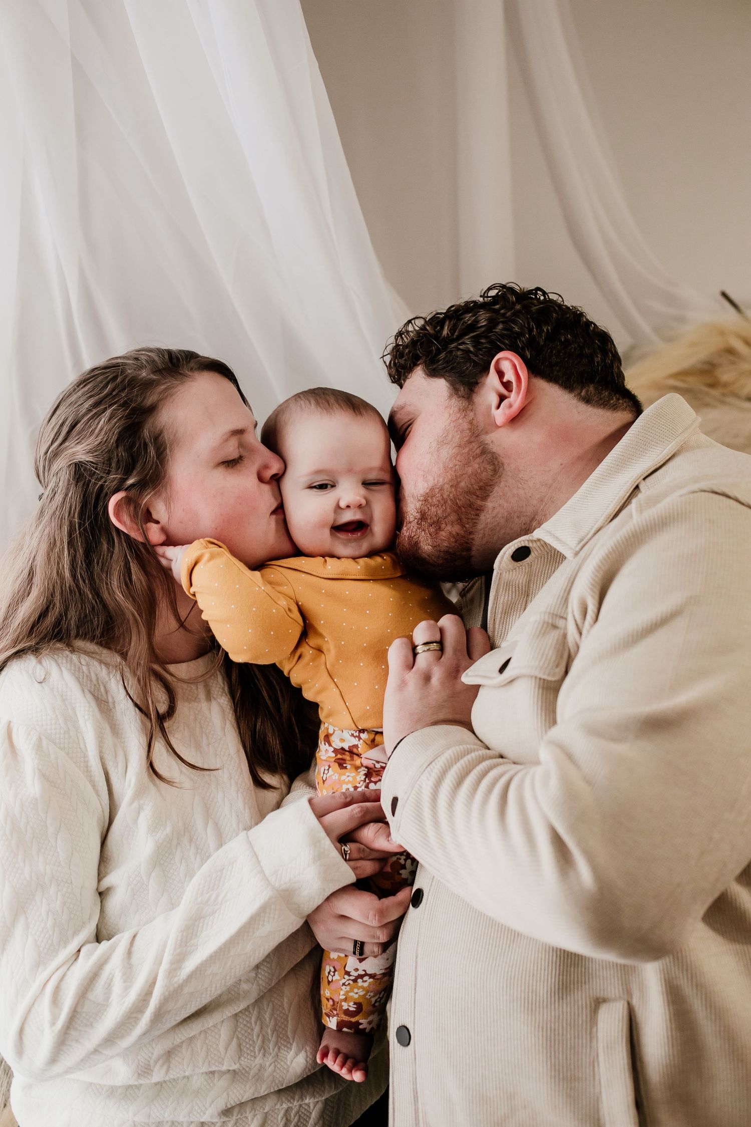Family sharing kisses and cuddles with baby in matching neutral outfits.