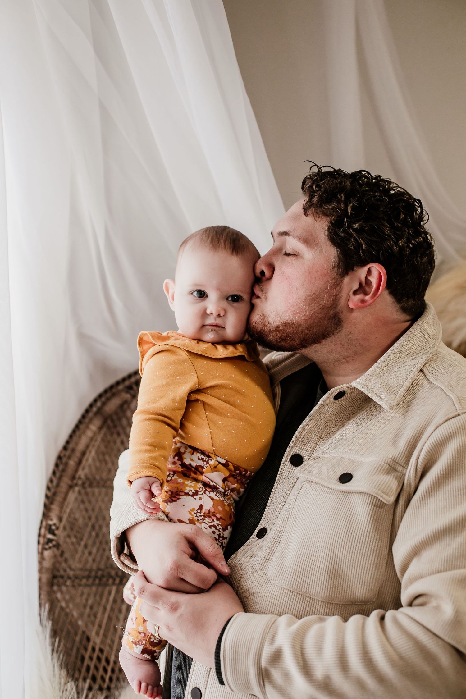 Sweet moments shared with baby in yellow outfit against white curtain backdrop.