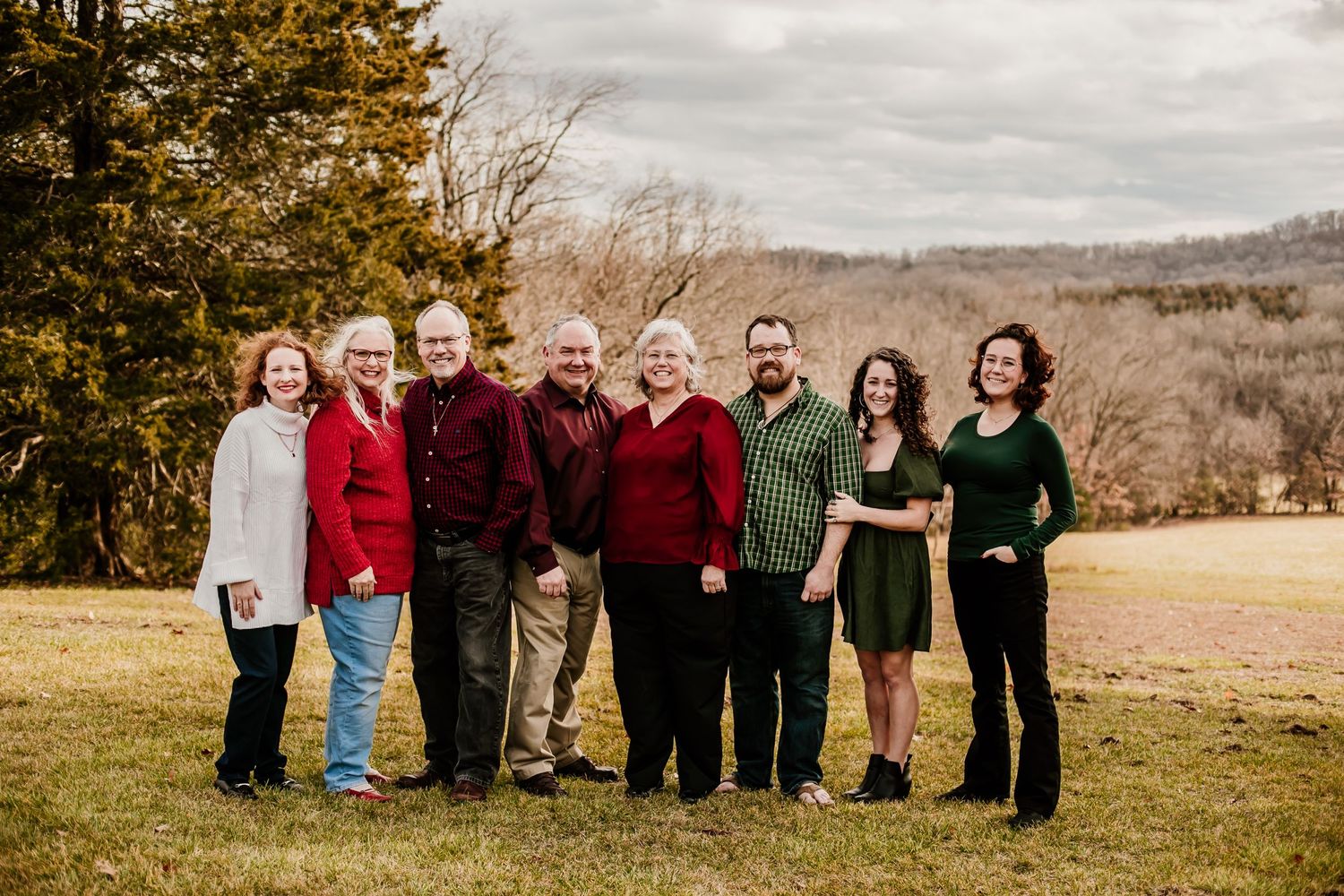 Extended family group photo outdoors with coordinated red and black attire against an autumn landscape.