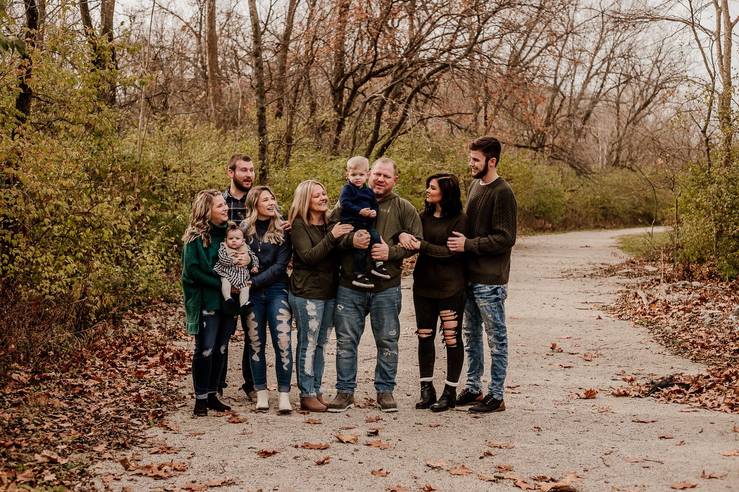 Extended family group posing together on path surrounded by fall foliage.