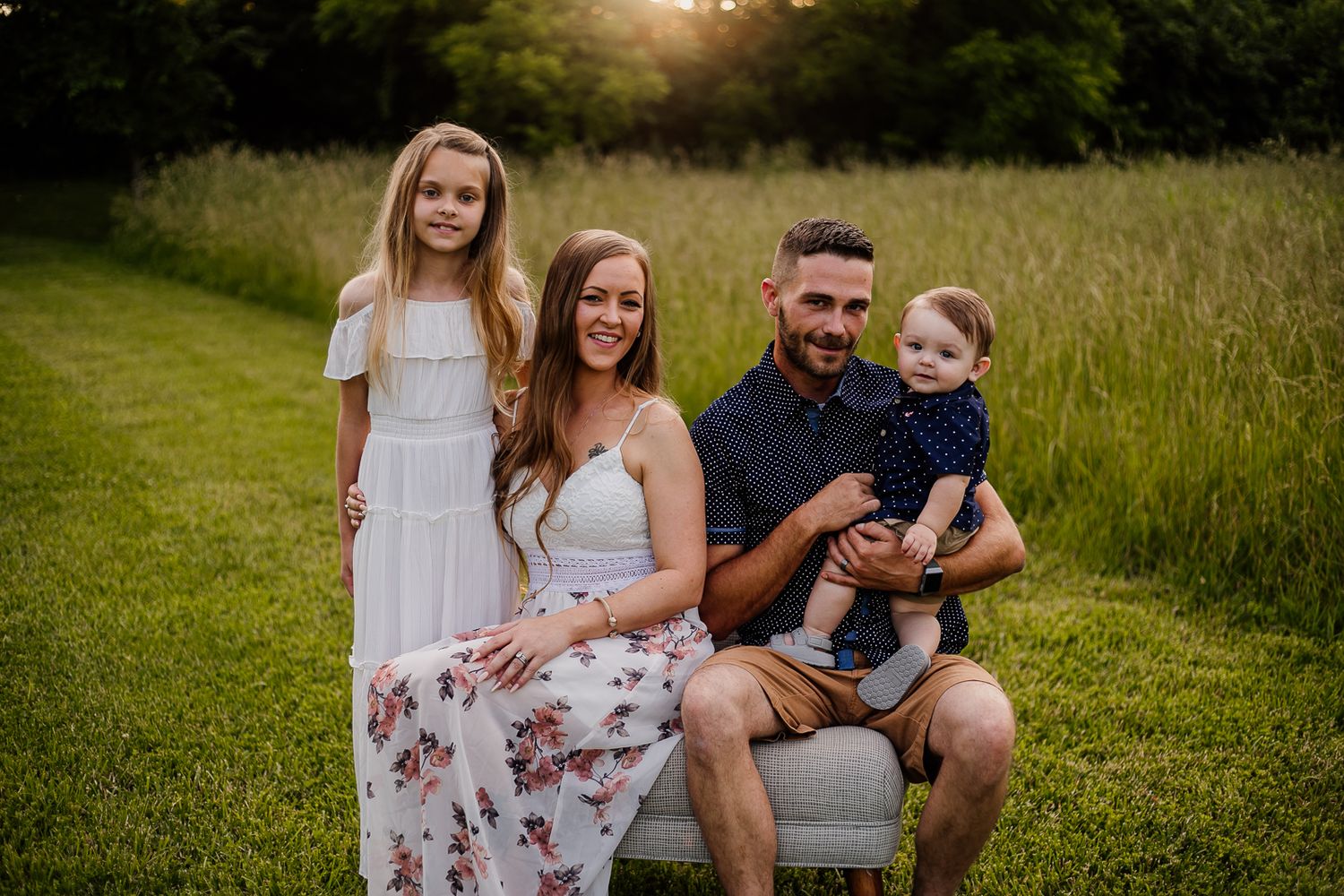 Family enjoying a sunset photoshoot in a tall grass field wearing coordinated casual outfits.