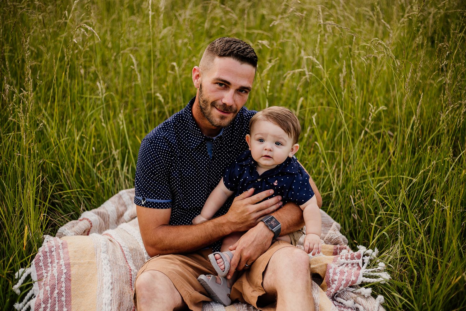Family relaxing on a blanket during an outdoor photo session in tall grass.