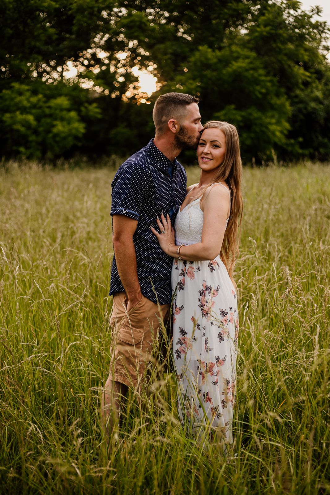 Couple sharing intimate moments during golden hour photoshoot in a meadow.