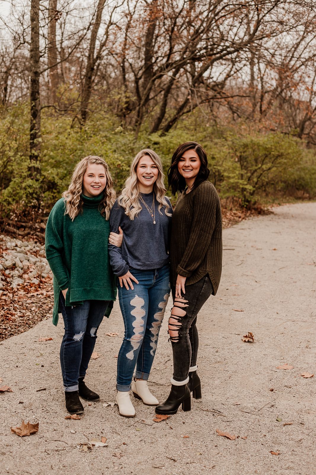 Three people posing casually on leaf-covered path in autumn setting.