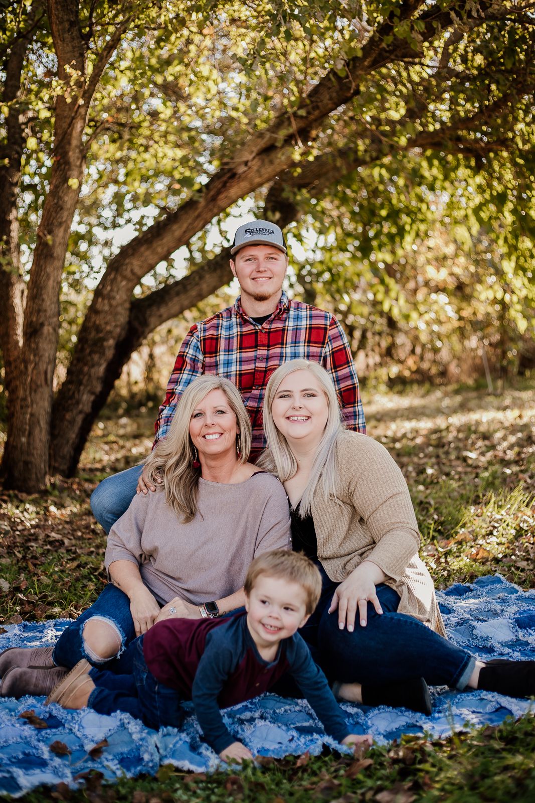 Family lounging on blue blanket under autumn trees during outdoor photography session.