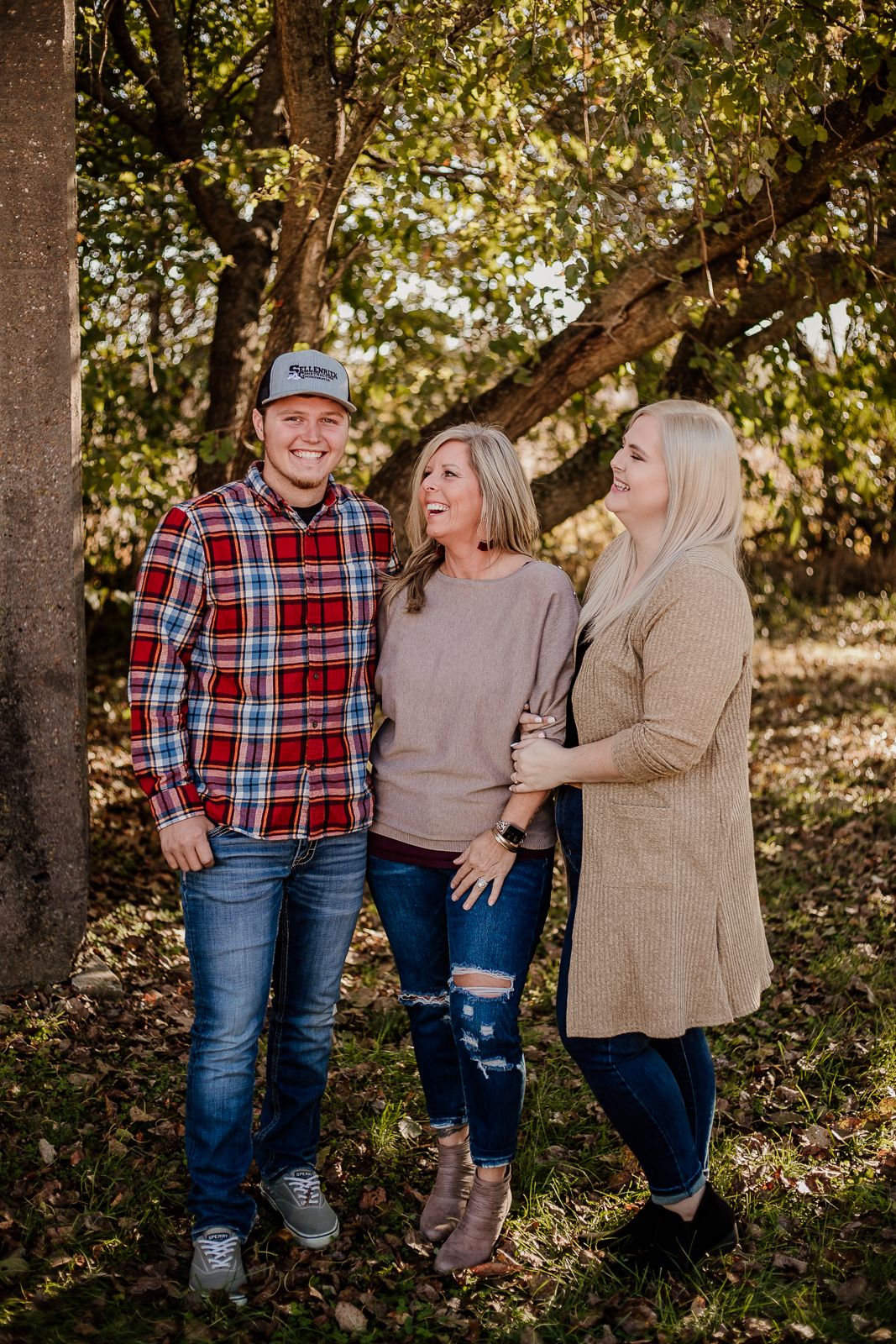 Group sitting casually under trees in coordinated fall outfits during outdoor photo session.