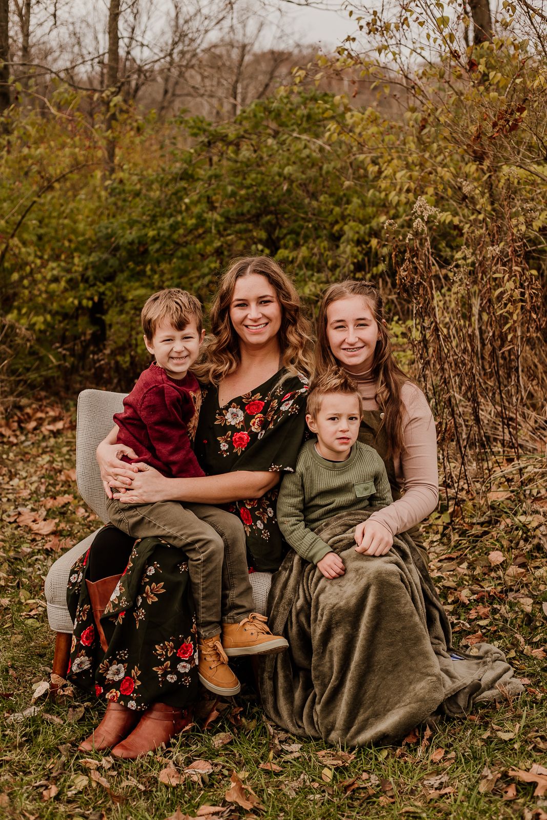 Family relaxing together on a blanket during an autumn outdoor photoshoot in warm earth-toned clothing.