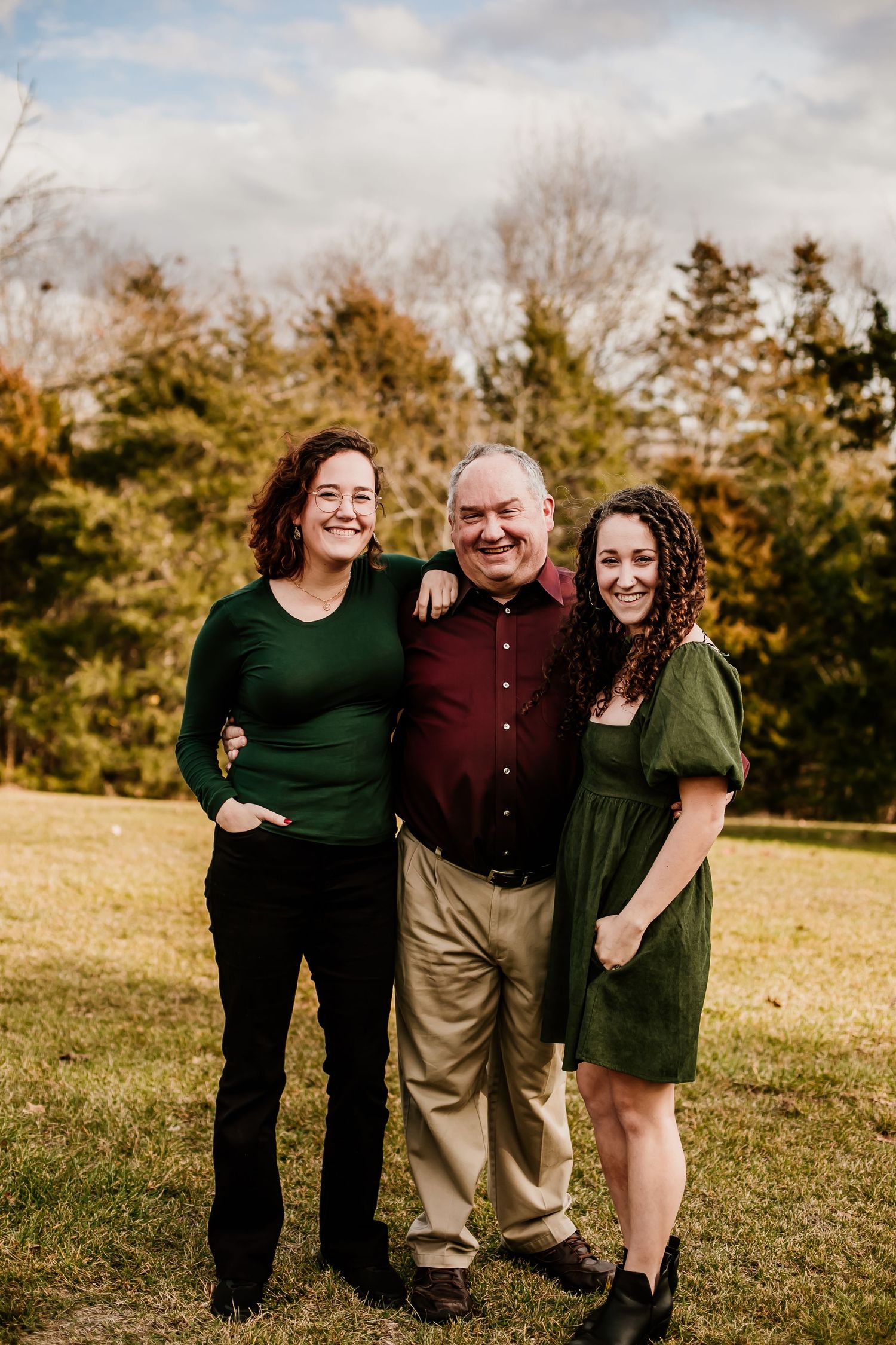 Family portrait in green and burgundy outfits standing together in an autumn field.
