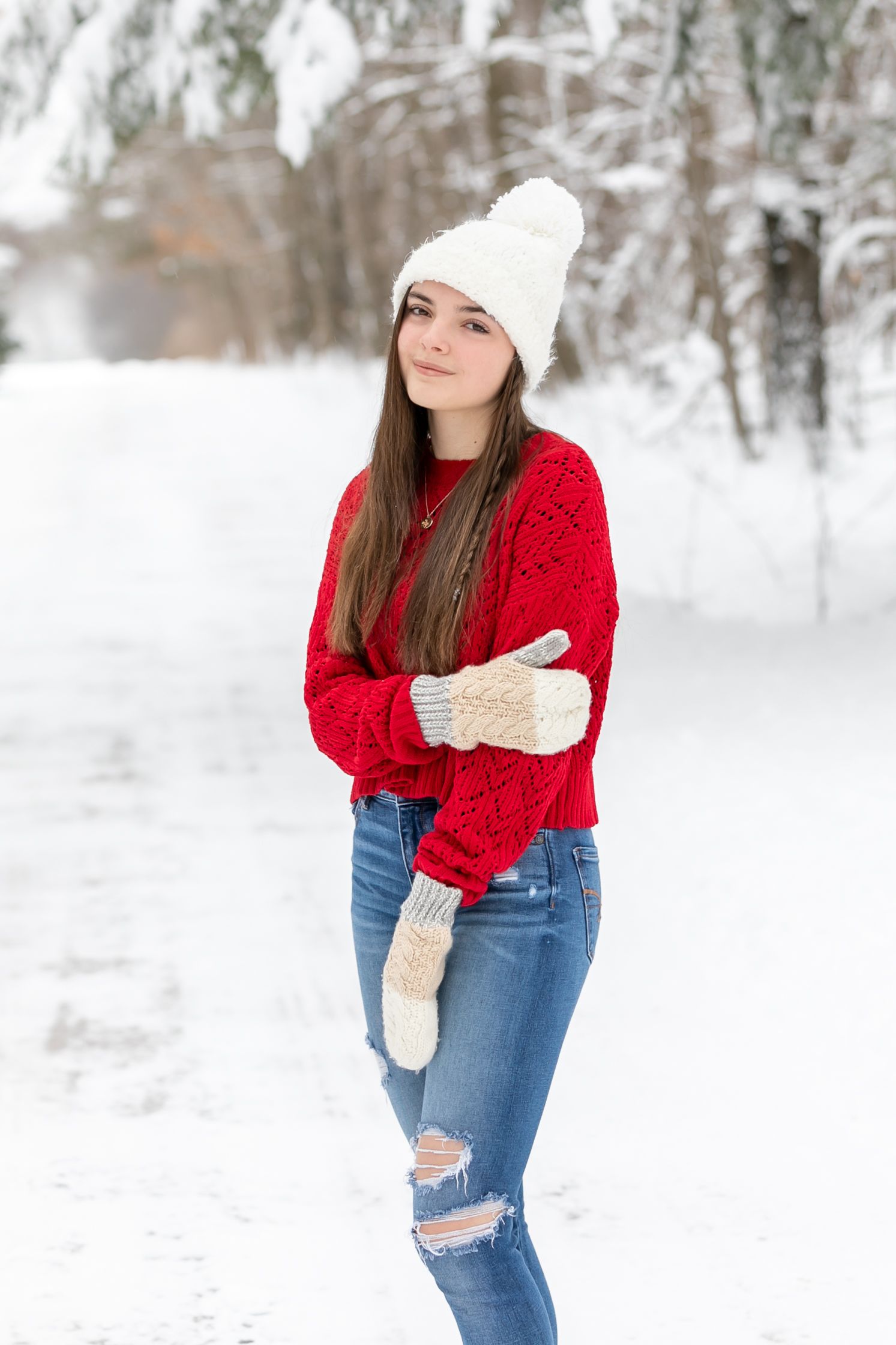 Winter portrait of person in red sweater and white beanie posing in snowy forest.