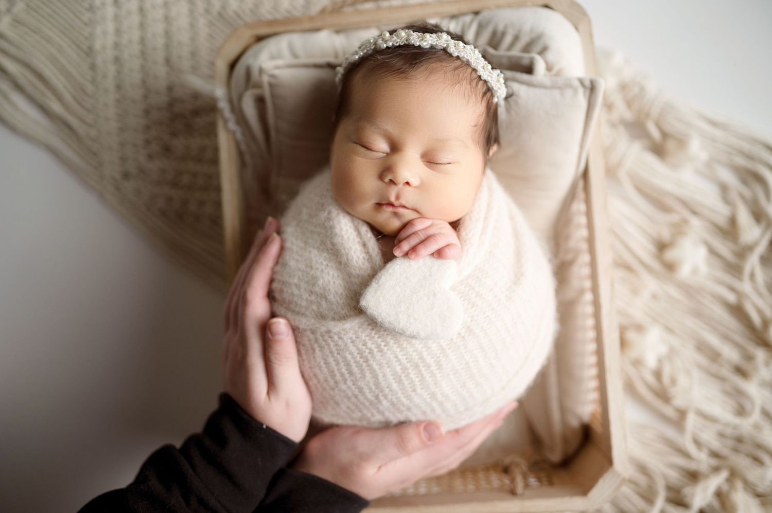 Peaceful newborn swaddled in light fabric resting on cream textured blanket.