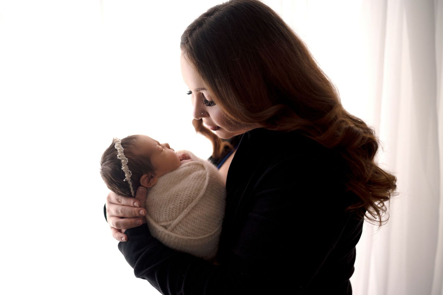 Parents in black clothing embracing their newborn against bright white wall.