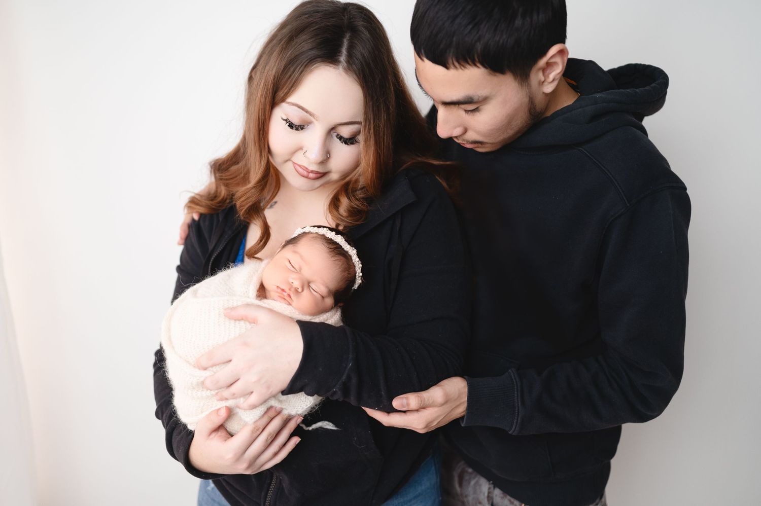 Intimate family moment with parents cuddling newborn in monochromatic setting.
